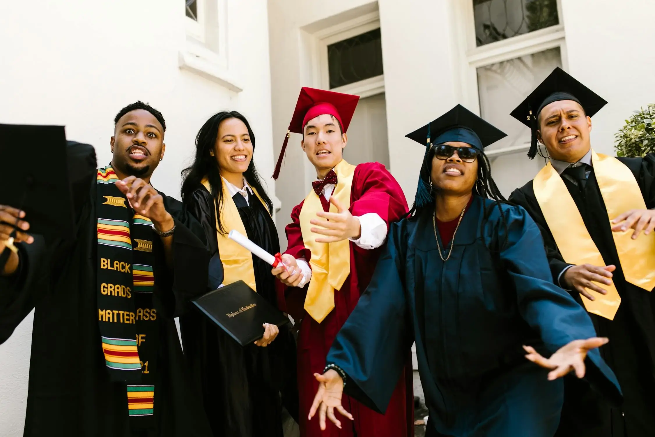 Five recent graduates in caps and gowns celebrate together, smiling and gesturing, symbolizing career beginnings
